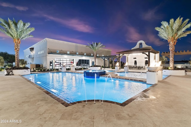 pool at dusk with an in ground hot tub, pool water feature, and a patio