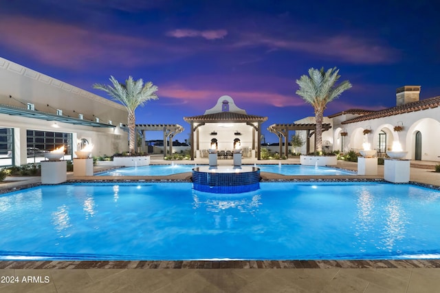 pool at dusk with a pergola, pool water feature, a hot tub, and a patio