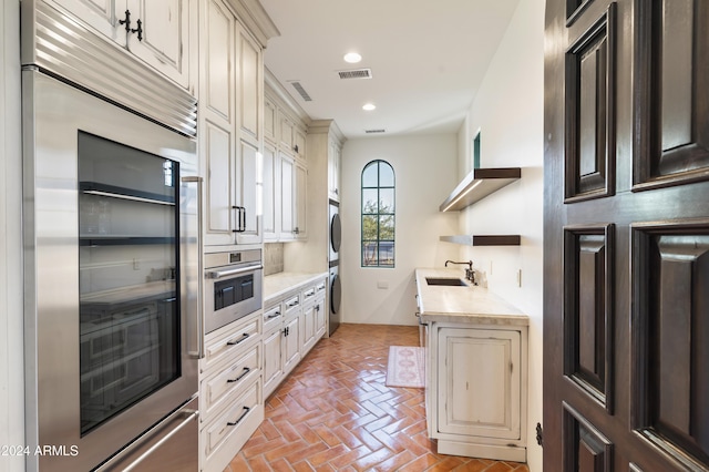 kitchen with stacked washer and dryer, appliances with stainless steel finishes, cream cabinetry, and sink