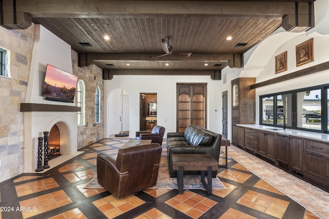 living room featuring ceiling fan, beam ceiling, a large fireplace, sink, and wooden ceiling