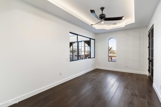 unfurnished room with ceiling fan, a tray ceiling, and dark hardwood / wood-style floors