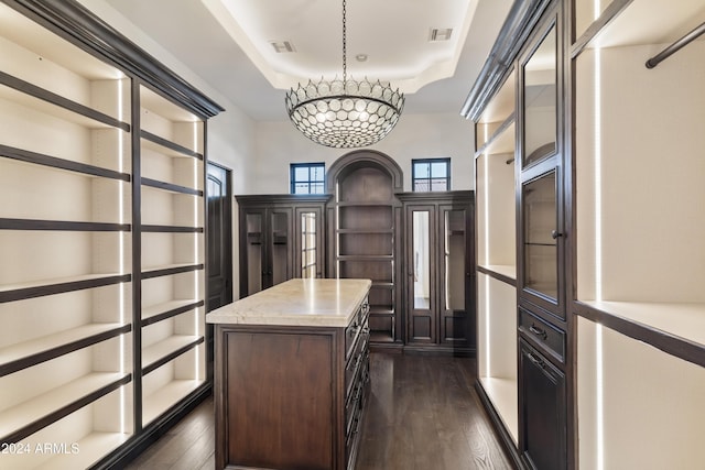 walk in closet featuring dark wood-type flooring, a tray ceiling, and a chandelier