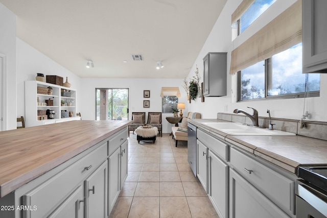 kitchen with a sink, stainless steel dishwasher, open floor plan, light tile patterned flooring, and butcher block counters