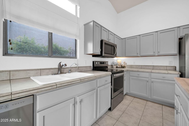 kitchen featuring light tile patterned floors, stainless steel appliances, a towering ceiling, and a sink