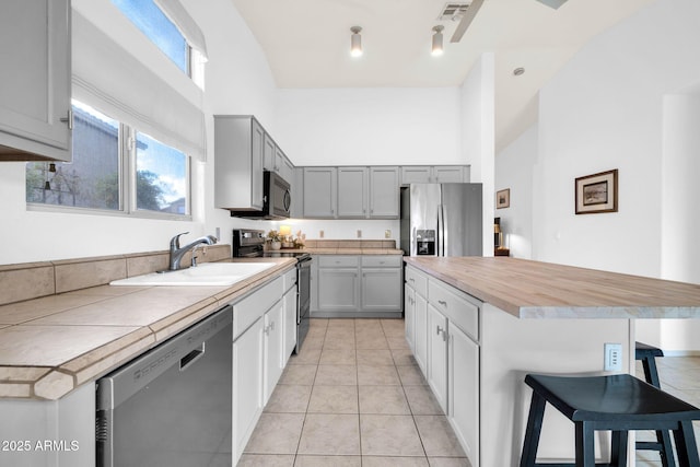 kitchen with a breakfast bar area, gray cabinets, a towering ceiling, stainless steel appliances, and a sink