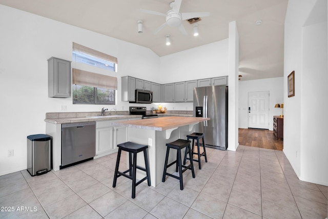 kitchen featuring visible vents, gray cabinets, appliances with stainless steel finishes, a kitchen breakfast bar, and a sink