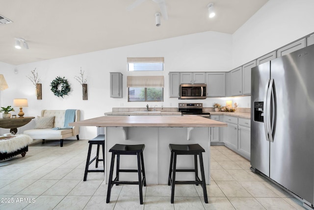 kitchen featuring gray cabinetry, a sink, wood counters, appliances with stainless steel finishes, and light tile patterned floors