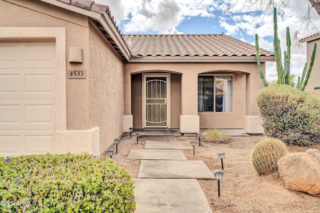 entrance to property featuring stucco siding, a tiled roof, and a garage