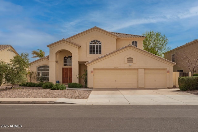 mediterranean / spanish home with a garage, driveway, a tiled roof, and stucco siding