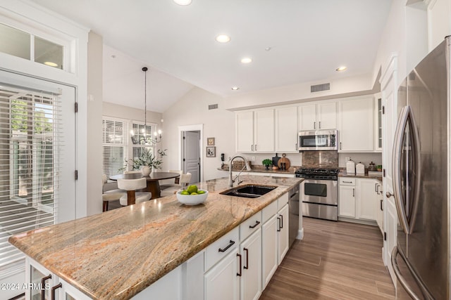 kitchen with sink, vaulted ceiling, light stone countertops, an island with sink, and appliances with stainless steel finishes