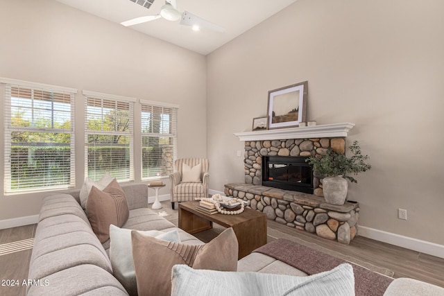 living room featuring hardwood / wood-style floors, high vaulted ceiling, a stone fireplace, and ceiling fan