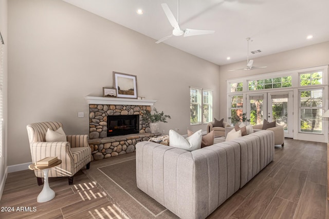 living room featuring french doors, a stone fireplace, ceiling fan, and dark wood-type flooring