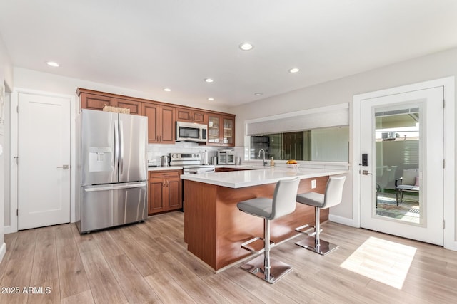 kitchen featuring appliances with stainless steel finishes, sink, backsplash, a kitchen breakfast bar, and light hardwood / wood-style flooring