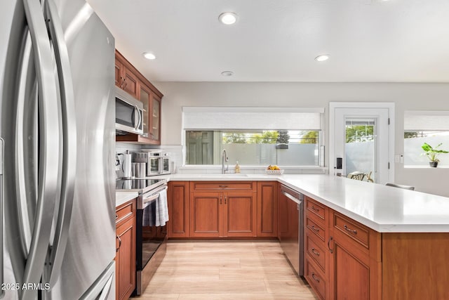 kitchen with sink, appliances with stainless steel finishes, light hardwood / wood-style floors, decorative backsplash, and kitchen peninsula