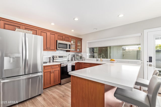 kitchen with a kitchen bar, sink, tasteful backsplash, appliances with stainless steel finishes, and light hardwood / wood-style floors