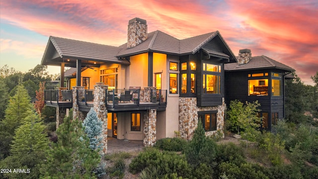 back house at dusk featuring ceiling fan, a balcony, and a patio area