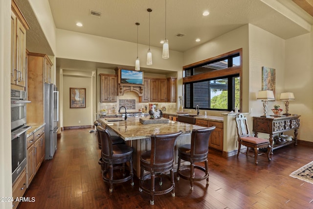 kitchen with light stone countertops, a kitchen island with sink, dark hardwood / wood-style floors, and pendant lighting