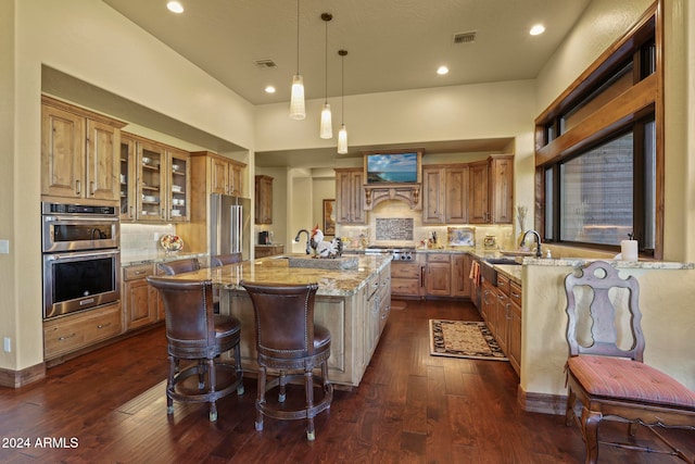 kitchen featuring light stone countertops, decorative backsplash, dark hardwood / wood-style flooring, hanging light fixtures, and a center island with sink