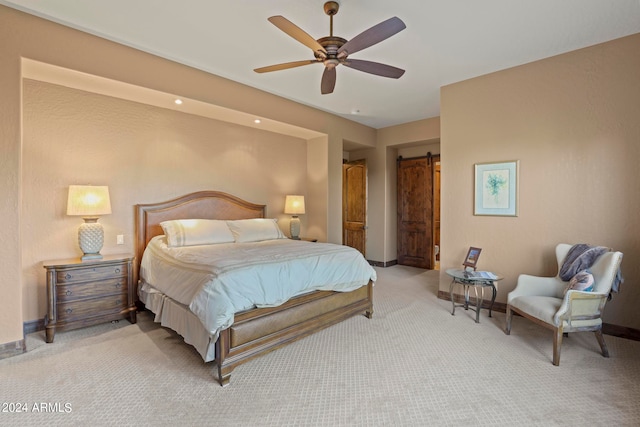 bedroom with ceiling fan, a barn door, and light colored carpet