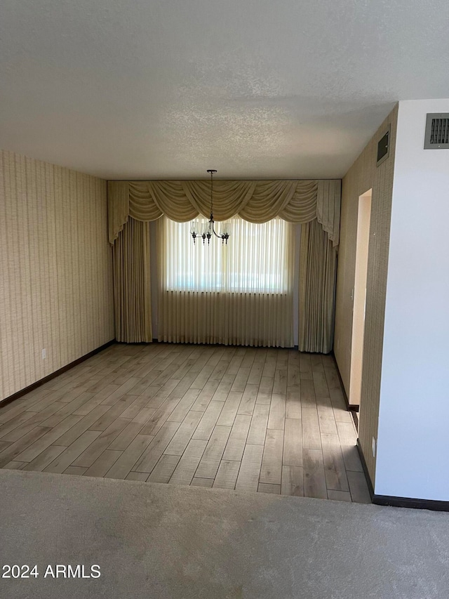 unfurnished room featuring a notable chandelier, hardwood / wood-style flooring, and a textured ceiling