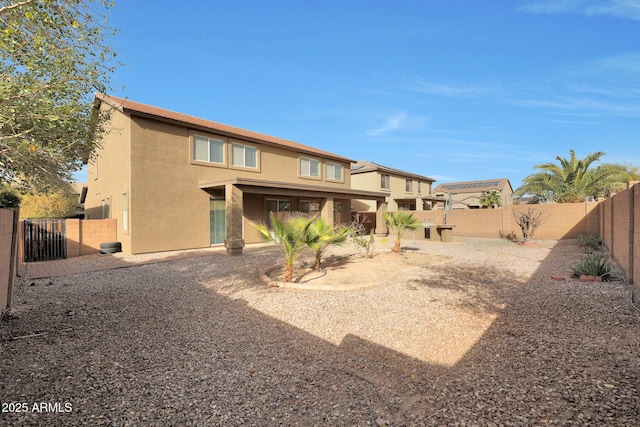 rear view of house featuring a fenced backyard and stucco siding