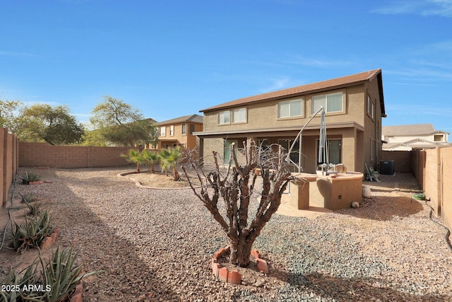 rear view of house featuring stucco siding, central AC unit, a patio area, exterior kitchen, and a fenced backyard