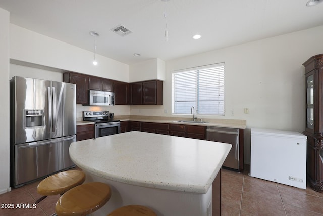 kitchen with stainless steel appliances, a sink, visible vents, dark brown cabinets, and a center island