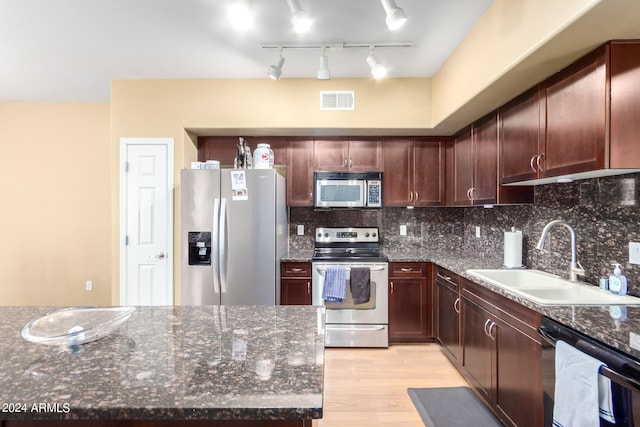 kitchen with decorative backsplash, light wood-type flooring, dark stone countertops, sink, and stainless steel appliances