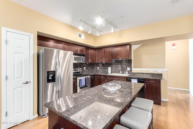 kitchen featuring appliances with stainless steel finishes, sink, a center island, light hardwood / wood-style floors, and dark stone counters