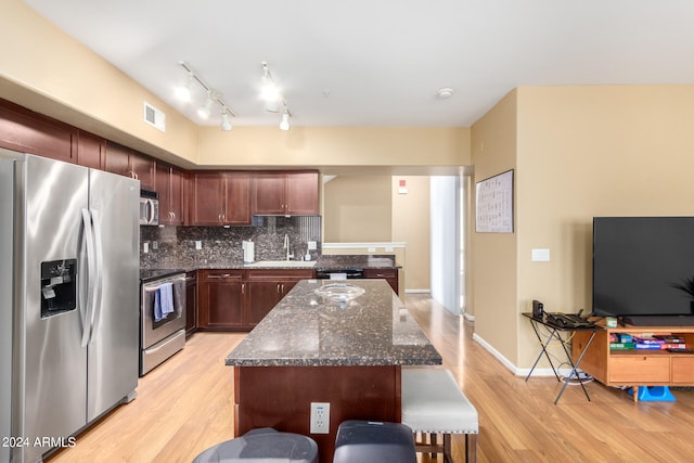 kitchen featuring dark stone counters, stainless steel appliances, sink, and light wood-type flooring