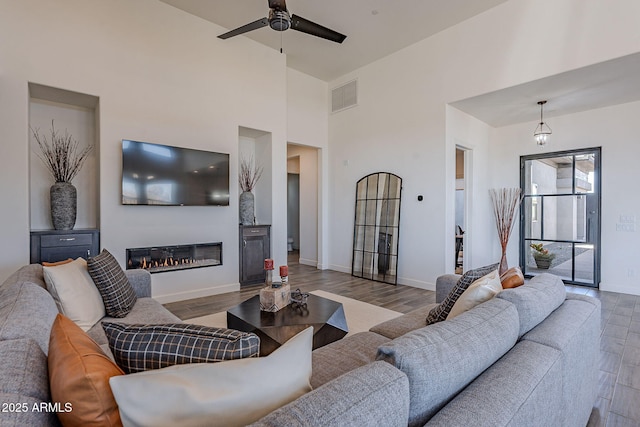 living room with light wood-type flooring, a towering ceiling, and ceiling fan