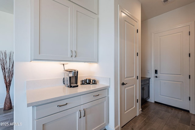 bar with white cabinets, light stone countertops, and dark hardwood / wood-style flooring