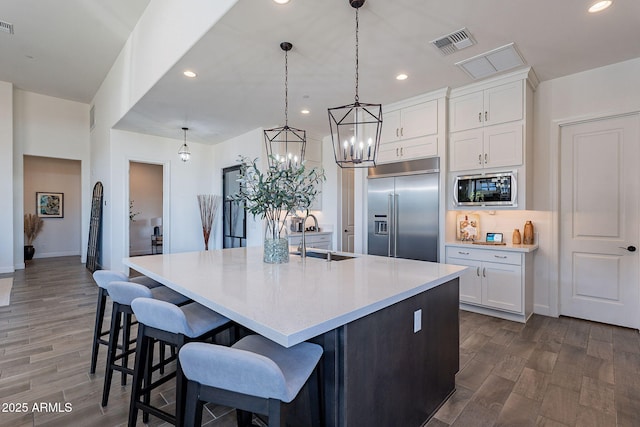 kitchen with a spacious island, pendant lighting, white cabinets, built in appliances, and sink