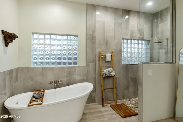 bathroom with shower with separate bathtub and tile walls