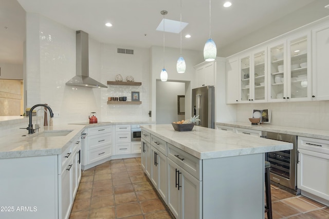 kitchen featuring wall chimney range hood, sink, white cabinetry, hanging light fixtures, and high quality fridge