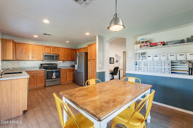 kitchen with hardwood / wood-style floors, appliances with stainless steel finishes, decorative light fixtures, and sink