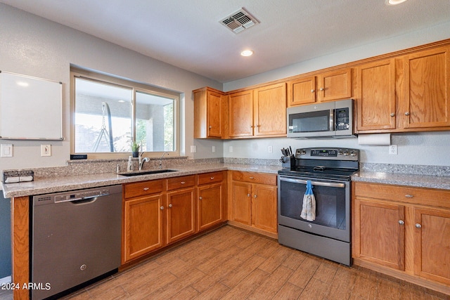 kitchen featuring light stone counters, sink, light hardwood / wood-style flooring, and appliances with stainless steel finishes