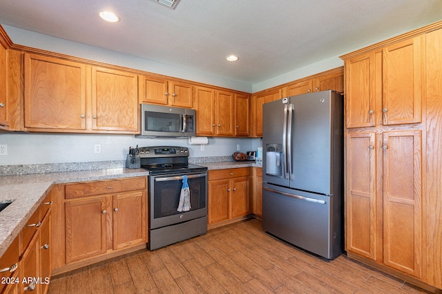 kitchen with light stone counters, light hardwood / wood-style floors, and appliances with stainless steel finishes