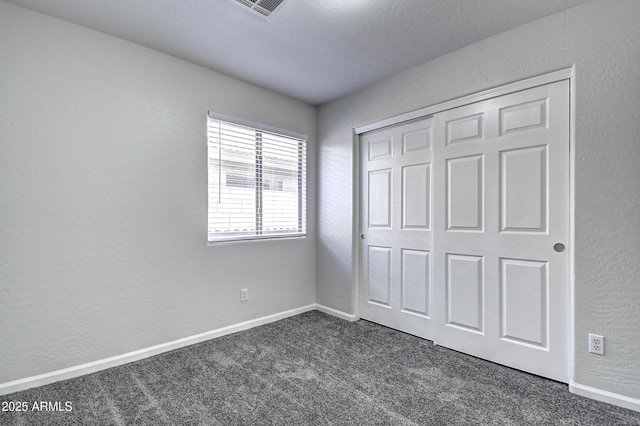 unfurnished bedroom with dark carpet and a closet