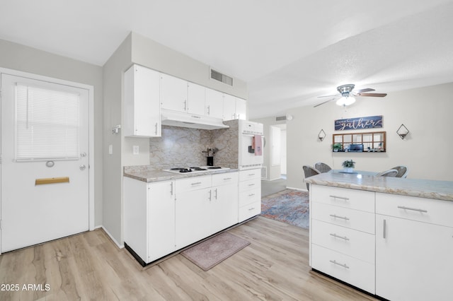 10873 W Clair Dr, Sun City, AZ 85351 - kitchen with under cabinet range hood, light wood-type flooring, tasteful backsplash, a ceiling fan, and white cabinetry