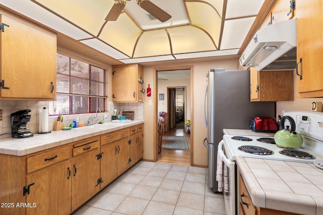 kitchen with tile countertops, white electric stove, tasteful backsplash, sink, and light tile patterned floors