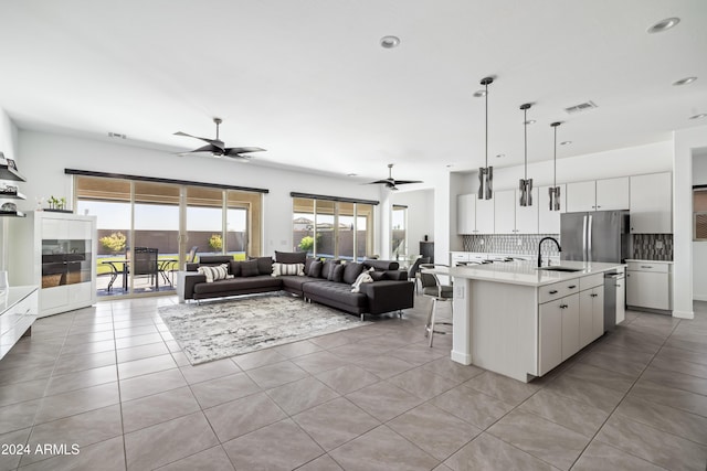 kitchen with backsplash, a kitchen island with sink, pendant lighting, white cabinetry, and light tile patterned flooring