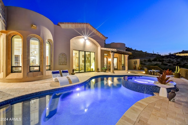 pool at dusk featuring an in ground hot tub and a patio area