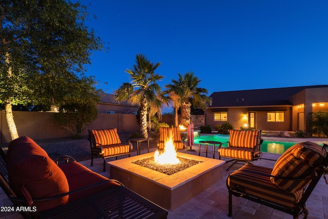 patio at night featuring a fenced in pool and an outdoor living space with a fire pit