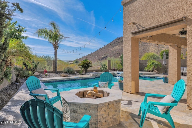 view of swimming pool with a mountain view, ceiling fan, pool water feature, and a fire pit