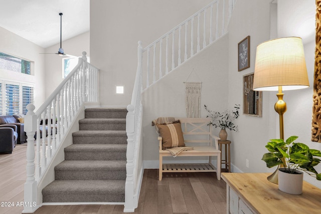 stairs with wood-type flooring, high vaulted ceiling, and ceiling fan