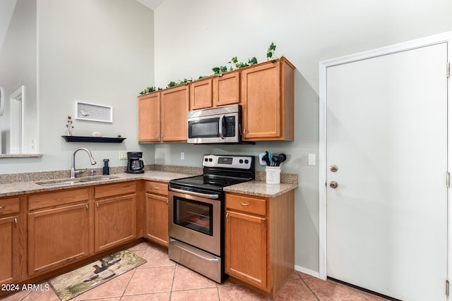 kitchen featuring light tile patterned floors, appliances with stainless steel finishes, brown cabinets, light stone counters, and a sink