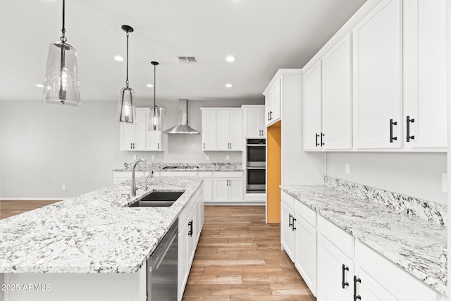 kitchen with white cabinets, sink, a center island with sink, and wall chimney range hood