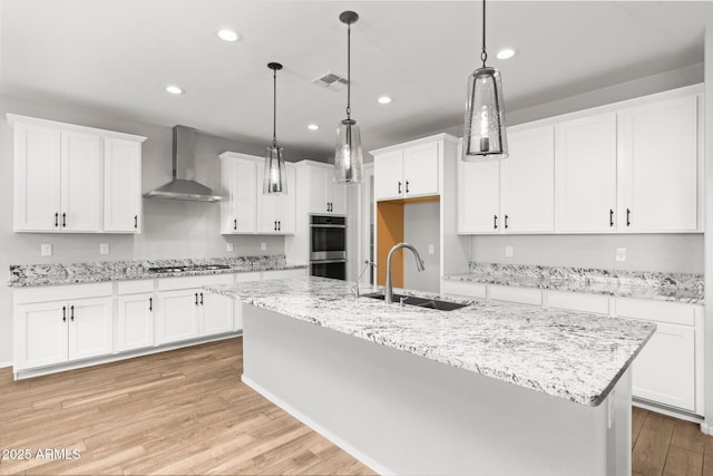 kitchen featuring an island with sink, sink, white cabinets, stainless steel appliances, and wall chimney exhaust hood