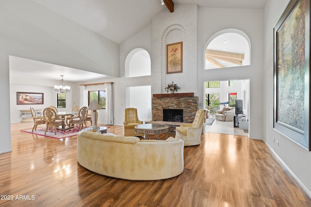 living room featuring beamed ceiling, light wood-type flooring, a stone fireplace, and high vaulted ceiling